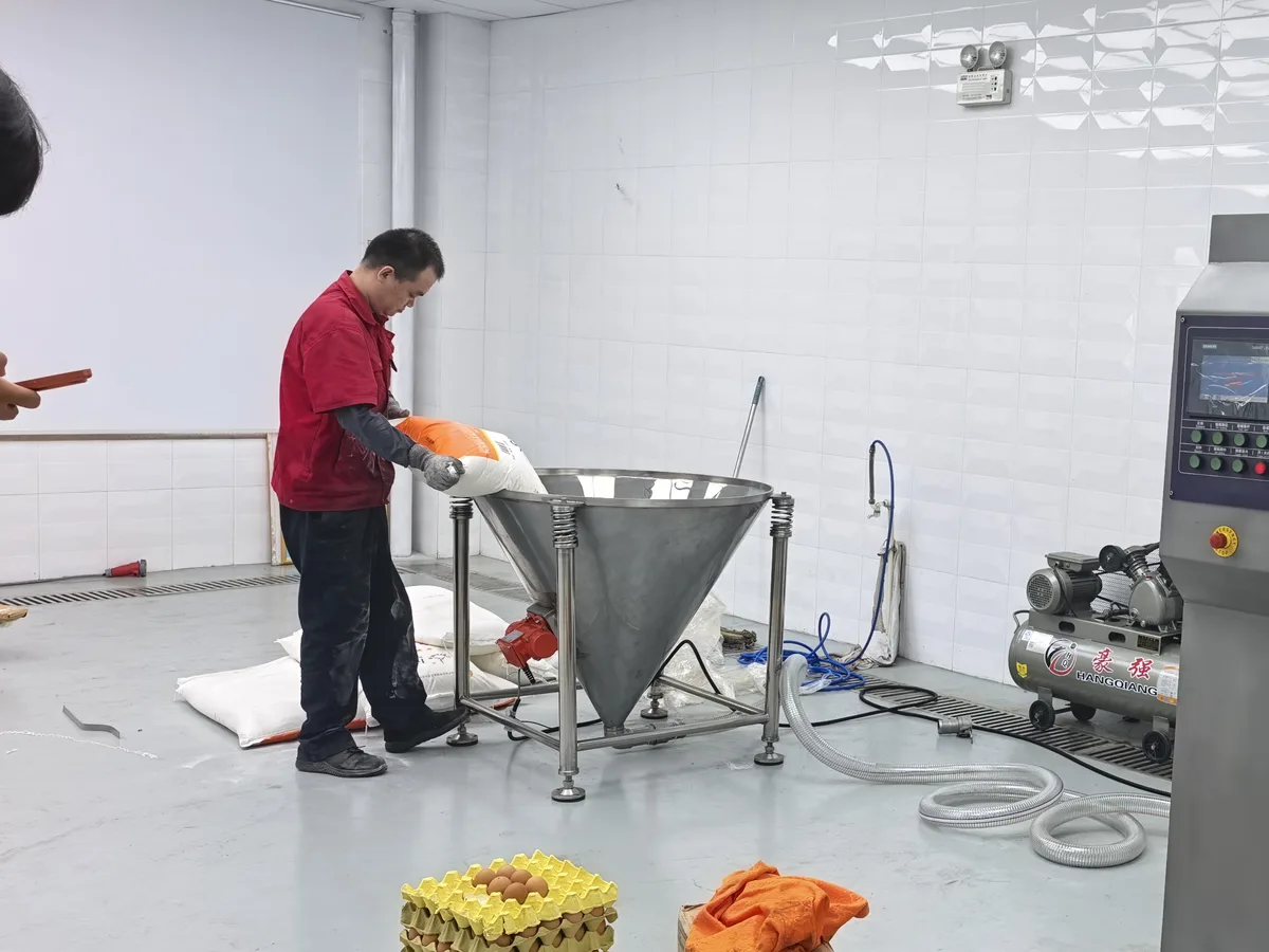 Operator loading the stainless flour suction hopper connected to the HM-300HP mixer during a factory test